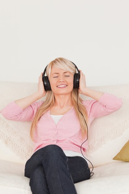 Schöne Frau, die Musik auf ihren Kopfhörern beim Sitzen auf einem Sofa hört