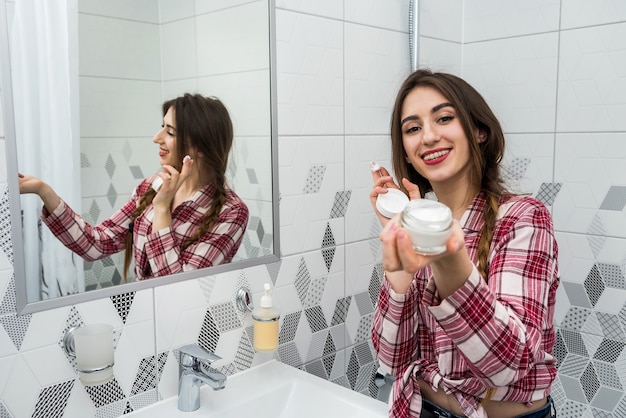 Schöne Frau, die reinigende feuchtigkeitsspendende Hautcreme auf Gesicht nach Bad badet. Hautpflege