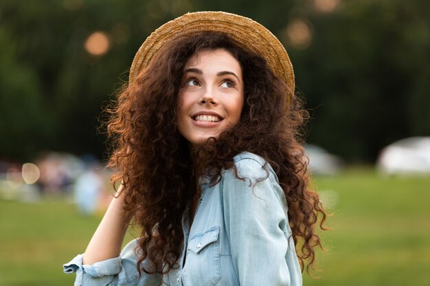 schöne Frau, die Strohhut lächelnd trägt, während sie im grünen Park geht