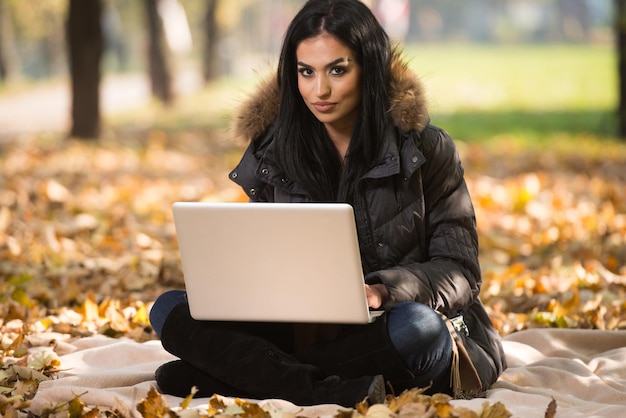 Schöne Frau, die während der Herbstsaison im Park am Laptop arbeitet