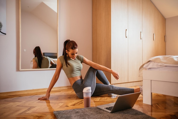 Schöne Frau, die zu Hause mit ihrem Laptop trainiert