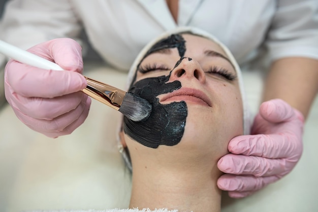 Schöne Frau erhält eine schwarze Gesichtsmaske in der Spa-Klinik für eine Spa-Behandlung und Hautpflege