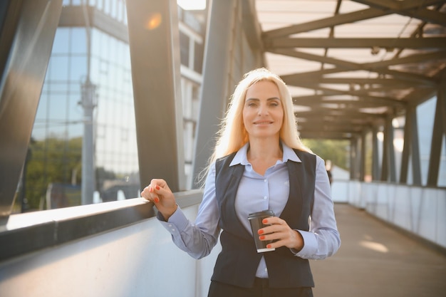 Schöne Frau gehen zur Arbeit mit Kaffee zu Fuß in der Nähe von Bürogebäude Porträt einer erfolgreichen Geschäftsfrau, die eine Tasse heißes Getränk hält