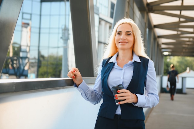 Schöne Frau gehen zur Arbeit mit Kaffee zu Fuß in der Nähe von Bürogebäude Porträt einer erfolgreichen Geschäftsfrau, die eine Tasse heißes Getränk hält