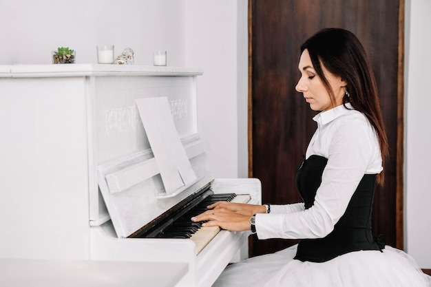 Schöne Frau gekleidet im weißen Hemd, das auf weißem Klavier spielt. Platz für Text oder Werbung