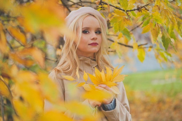 Schöne Frau hält im Herbst gelbe Blätter im Freien auf dem Hintergrund der Herbstnatur