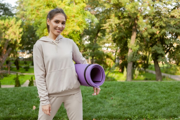 Schöne Frau hält Matte für Sportübungen in den Händen vor dem Training im Freien