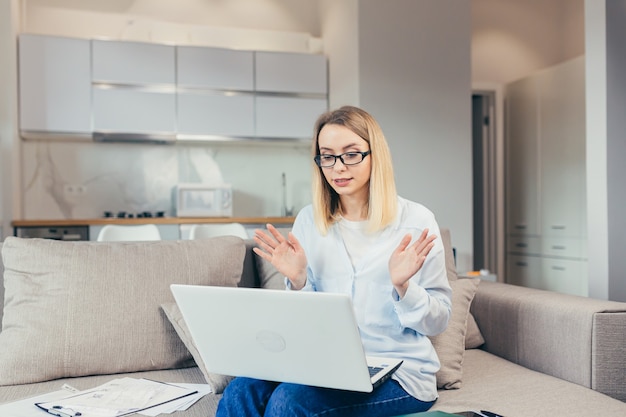 Schöne Frau hält Online-Beratung mit Laptop auf dem Sofa zu Hause sitzen