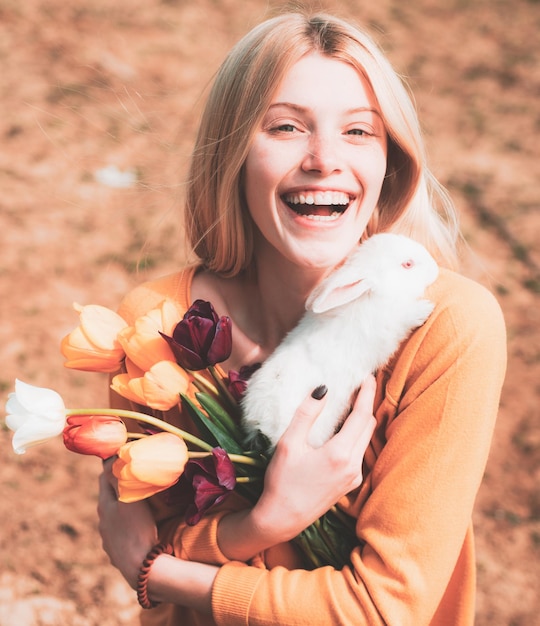 Schöne Frau hält weißes Kaninchenporträt einer jungen Frau, die mit Kaninchen fröhliche Ostern posiert