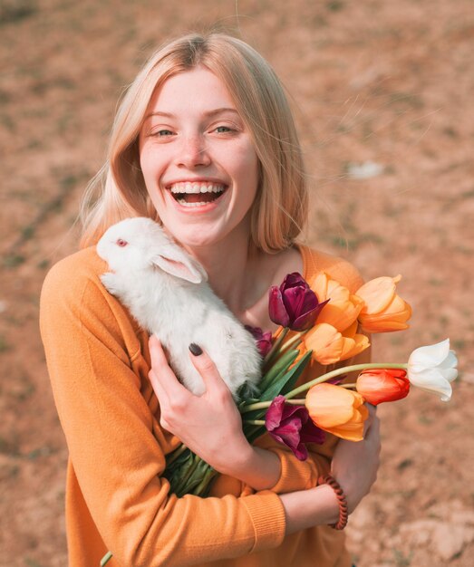 Schöne Frau hält weißes Kaninchenporträt einer jungen Frau, die mit Kaninchen fröhliche Ostern posiert