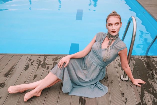 schöne Frau im grauen Cocktailkleid, das fast Swimmingpool legt