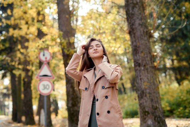 Schöne Frau im grünen Kleid, das im Herbstpark mit gelben Blättern aufwirft