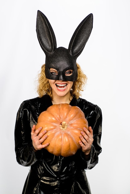 Schöne Frau im Halloween-Häschenkostüm hält sexy blondes Mädchen des Kürbises in der schwarzen Maske des Kaninchens mit