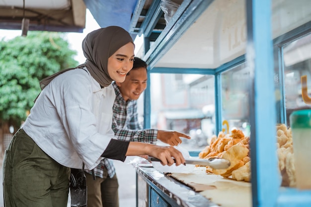 Schöne Frau im Hijab, während sie verschiedene Arten von frittierten Speisen mit einem Karren am Straßenrand verkauft