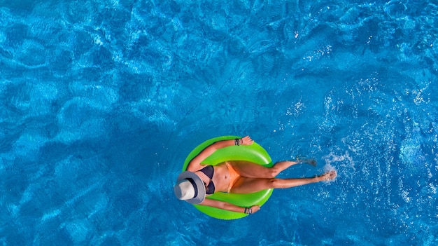 Schöne Frau im Hut in der Luftaufnahme des Schwimmbades von oben, junges Mädchen im Bikini entspannt und schwimmt auf aufblasbarem Ringkrapfen und hat Spaß im Wasser im Urlaub