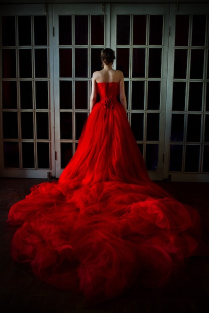 Schöne Frau im langen roten Kleid und in der königlichen Krone, die in der Nähe der Retro-Tür mit Buntglas steht