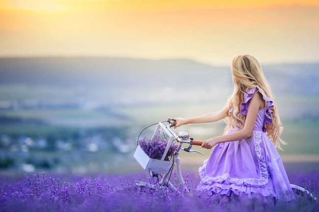 Schöne Frau im lila Kleid führt ein Fahrrad durch ein Lavendelfeld