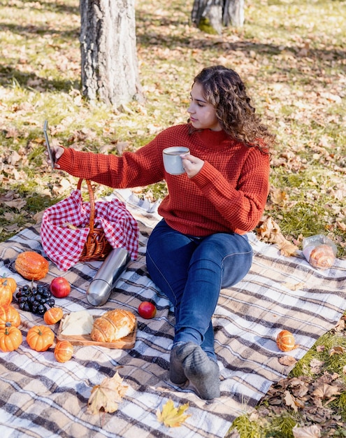 Schöne Frau im roten Pullover auf einem Picknick in einem Herbstwald mit Handy