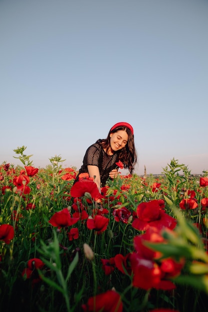 Schöne Frau im schwarzen Kleid bei Sonnenuntergang auf dem Mohnblumenfeld