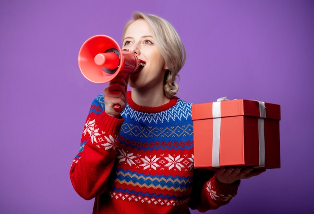 Schöne Frau im Weihnachtspullover mit Geschenkbox und Megaphon