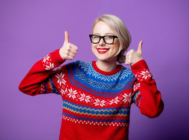 Schöne Frau im Weihnachtspullover und in den Gläsern auf lila Hintergrund