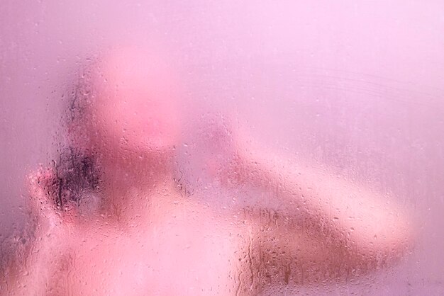 Schöne Frau in der Dusche hinter Glas mit Tropfen rosa Glanz