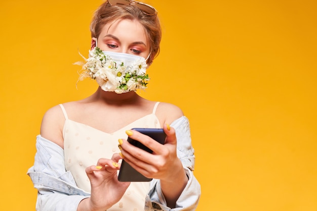 Schöne Frau in der medizinischen Maske mit Blumenentwurf, Telefon haltend