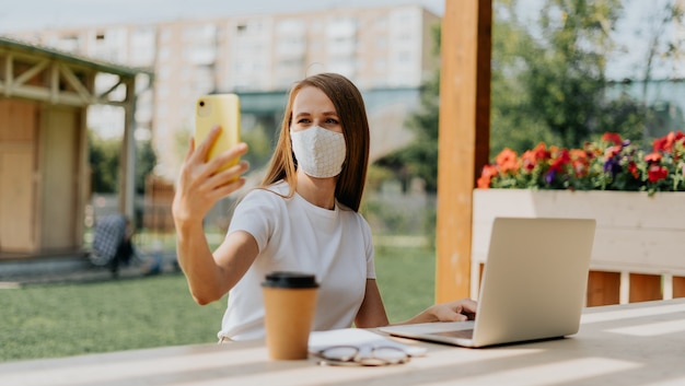 Schöne Frau in der medizinischen schützenden Gesichtsmaske, die ein selfie nimmt