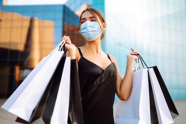 Schöne Frau in der sterilen medizinischen Schutzmaske mit Einkaufstaschen nahe Einkaufszentrum.