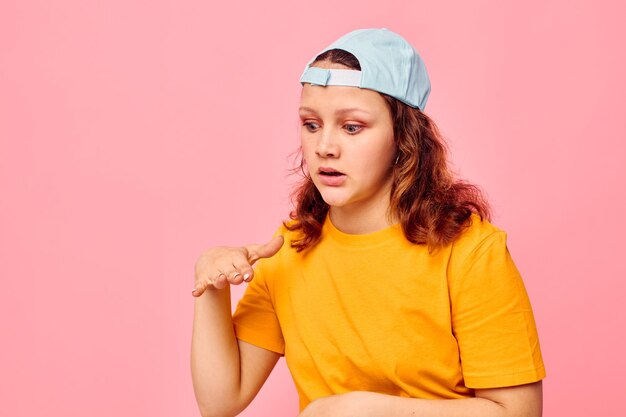 Schöne Frau in einem gelben T-Shirt und einer blauen Kappe, die Emotionen aufwirft, rosa Hintergrund unverändert