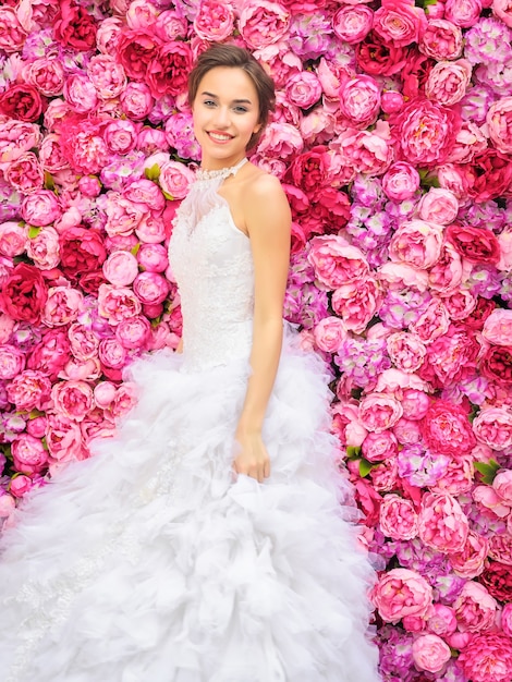 Schöne Frau in einem Hochzeitskleid auf einer Blumenwand