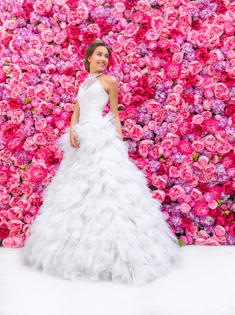 Schöne Frau in einem Hochzeitskleid auf einer Blumenwand