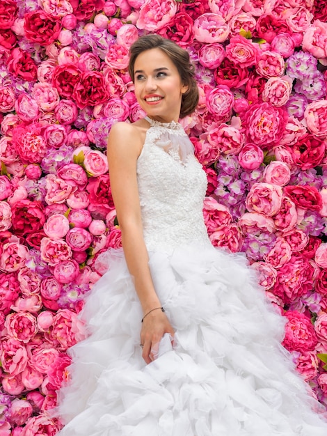 Schöne Frau in einem Hochzeitskleid auf einer Blumenwand