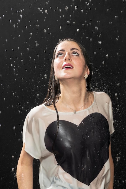 Foto schöne frau in einem nassen t-shirt, das am körper klebt, blickt auf den regen, nahaufnahme, auf schwarzem hintergrund