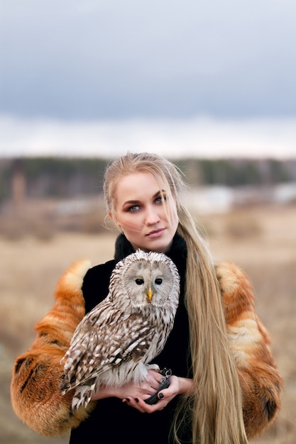 Schöne Frau in einem Pelzmantel mit einer Eule auf seinem Arm. Blond