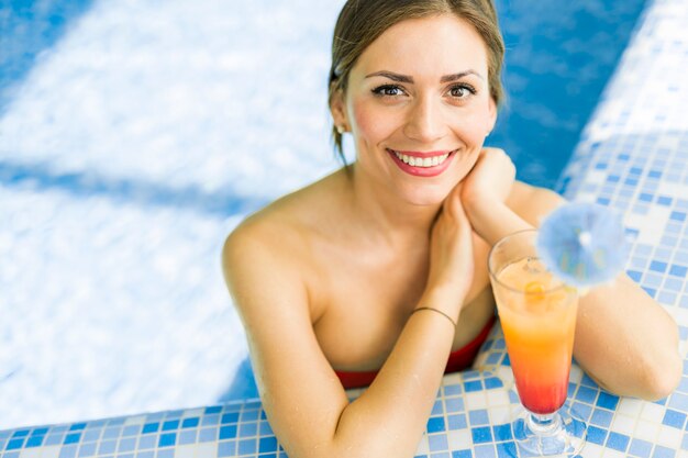 Schöne Frau in einem Pool mit einem Cocktail neben ihr