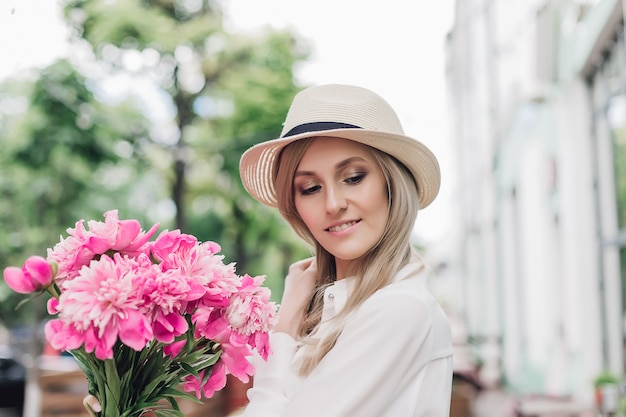 Schöne Frau in einem Sommerhut, der Blumen hält