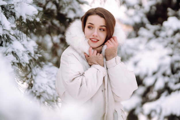 Schöne Frau in einem verschneiten Park. Junge Dame, die an einem sonnigen Wintertag spaziert.