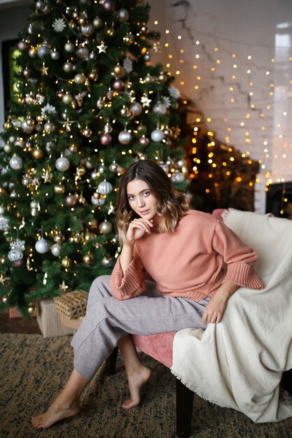 schöne Frau in einem warmen Pullover sitzt am Weihnachtsbaum