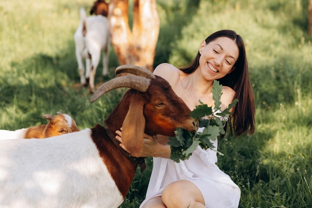 Schöne Frau in einem weißen Kleid füttert Ziegen und ihre Kinder Grün auf einer Öko-Farm.