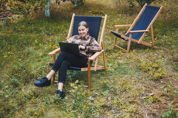 Schöne Frau in kariertem Hemd mit Laptop, die draußen im Garten-Home-Office-Konzept arbeitet Fernarbeit