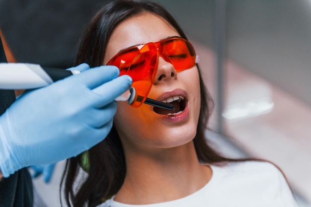 Schöne Frau in roter Schutzbrille hat einen Besuch in der Zahnarztpraxis. Konzeption der Stomatologie.