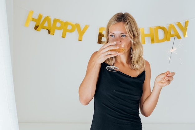 Schöne Frau in stilvollem schwarzem Kleid feiert Geburtstag und trinkt Champagner