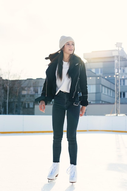 Schöne Frau in stylischer Jacke, die Spaß hat, auf der Eislaufbahn im Freien zu lachen, fröhlich, ziemlich jung