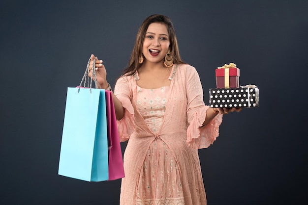 Schöne Frau in traditioneller indischer Kleidung mit Einkaufstüten und Geschenkbox auf grauem Hintergrund