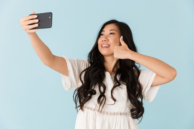 Schöne Frau isoliert über blaue Wand nehmen ein Selfie per Handy