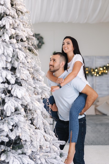 Schöne Frau kletterte hinter ihren Ehemännern zurück, um den Weihnachtsbaum zu schmücken. Süßes Paar verbrachte Zeit
