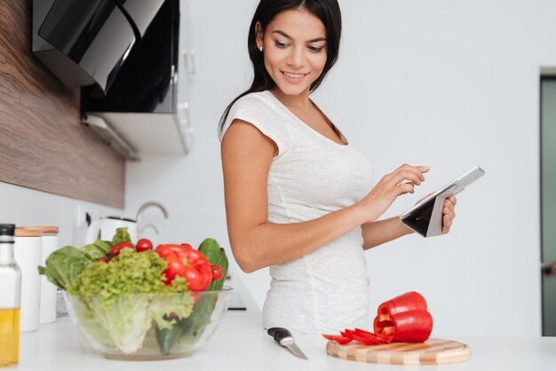 Schöne Frau liest Rezept vom Tablet-Computer in der Küche. Produkte anschauen.