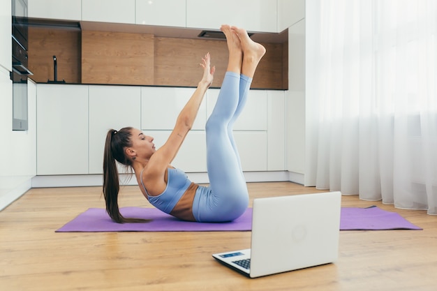 schöne Frau macht Fitness zu Hause online mit Laptop