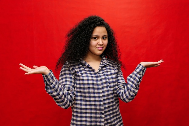 Schöne Frau mit Afro-Haar macht Geste mit ihrem Gesicht und ihren Händen, auf einem roten Hintergrund.